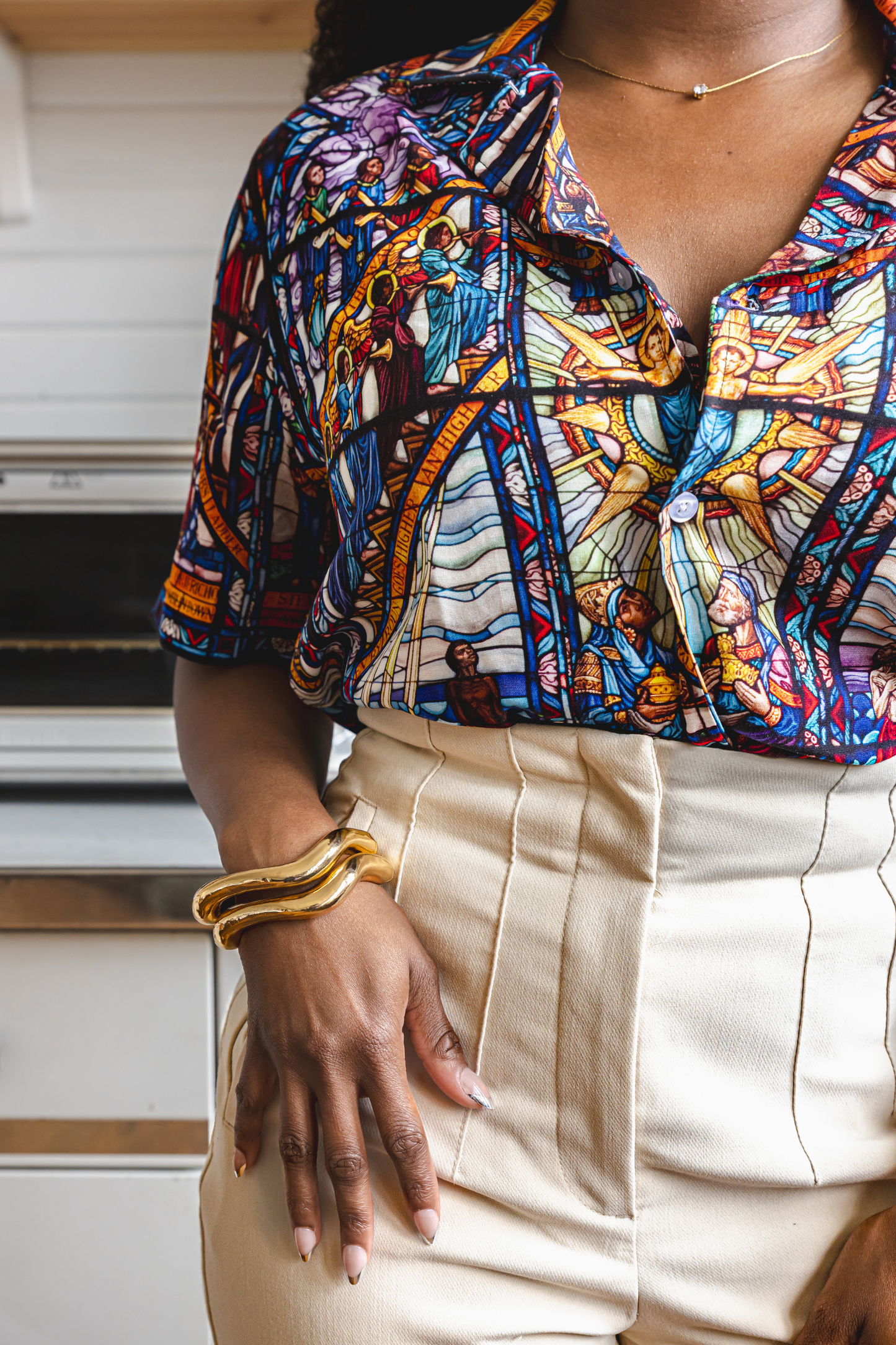 Close up of female model wearing a camp collar shirt with a pattern inspired by the Tuskegee University Chapel's "singing windows" stained glass installation, standing in a room with light-colored walls.