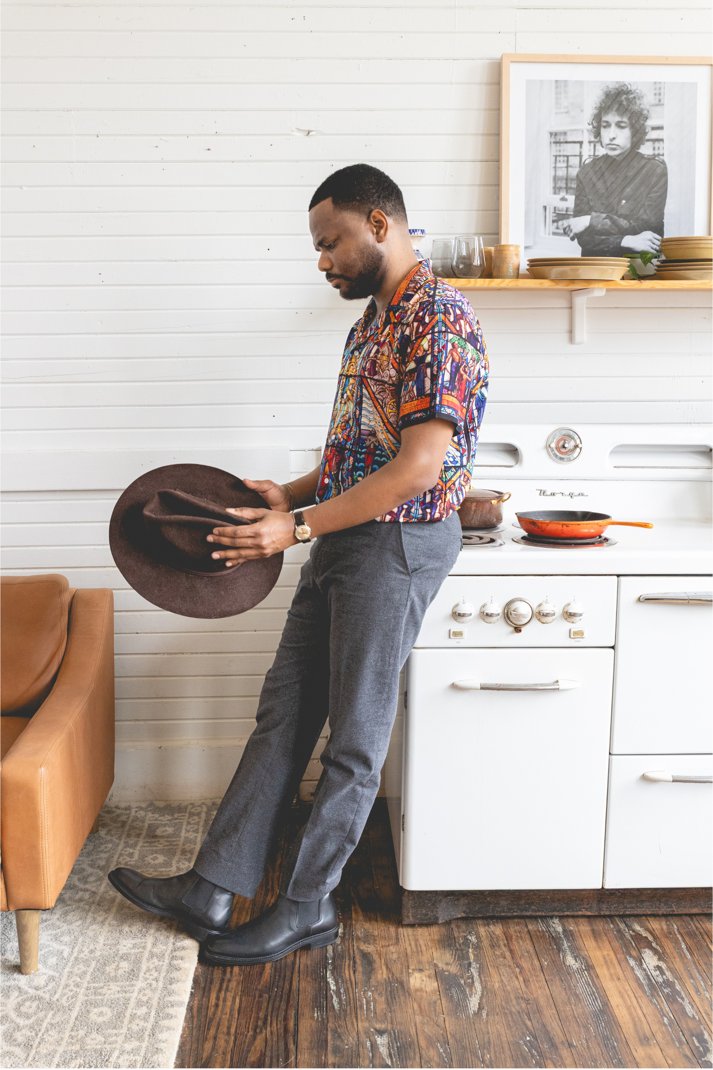A male model wearing a camp collar shirt with a pattern inspired by the Tuskegee University Chapel's "singing windows" stained glass installation, standing in a room with light-colored walls.