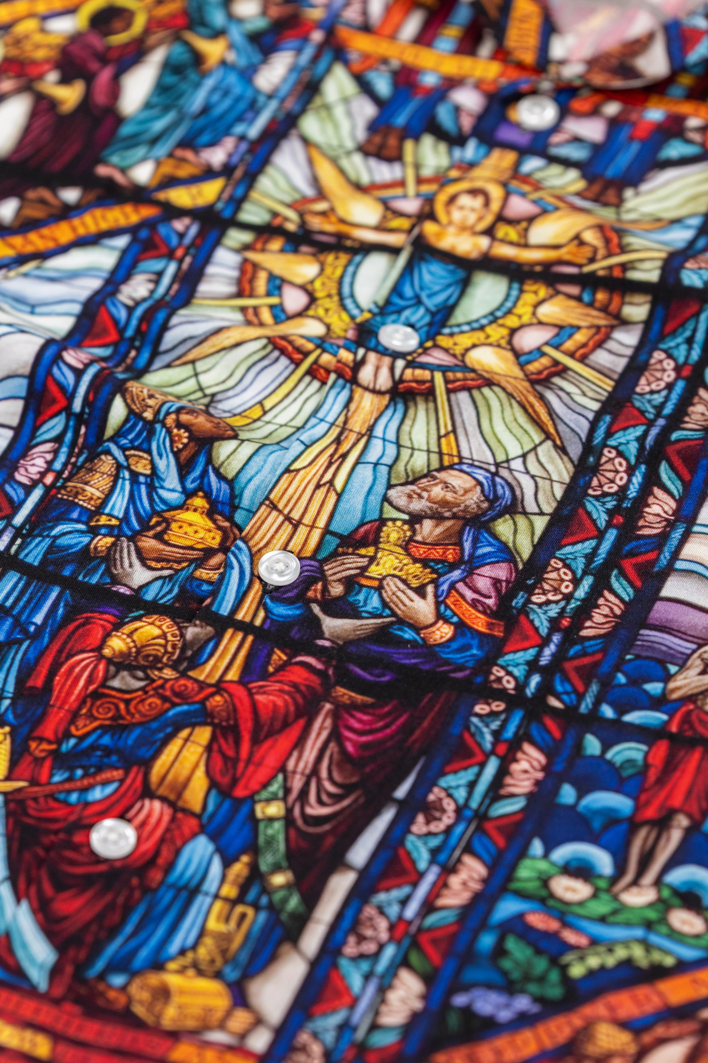 Close up shot of camp collar viscose shirt with a pattern inspired by the Tuskegee University Chapel's "singing windows" stained glass installation, standing in a room with light-colored walls.