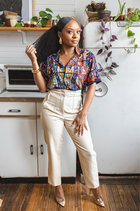 A female model wearing a camp collar shirt with a pattern inspired by the Tuskegee University Chapel's "singing windows" stained glass installation, standing in a room with light-colored walls.